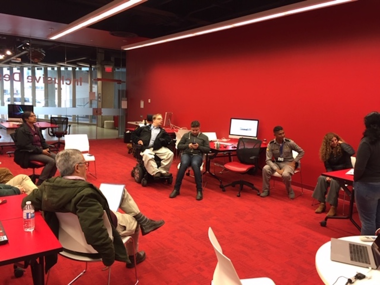 A photo of people sitting in a circle in a room with a red wall and red carpet.