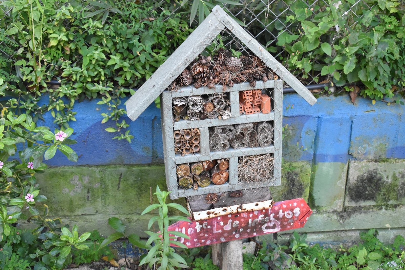 A small house shaped structure with sections that are filled with various materials such as tiny bricks, pinecones and sticks where bees can nest.