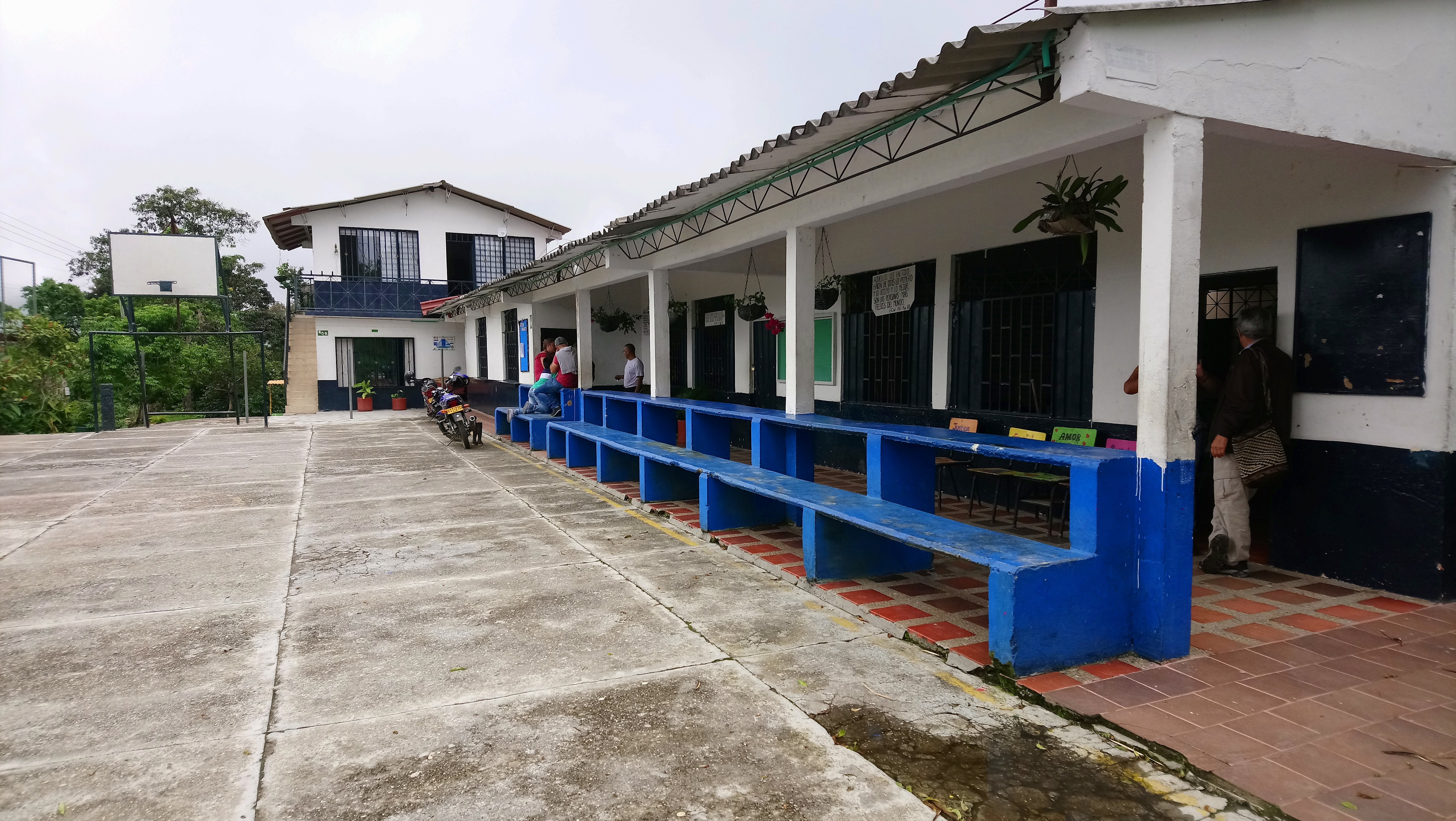 A blue and white school entrance. Some people appear in the back of the image. The sky looks white. 